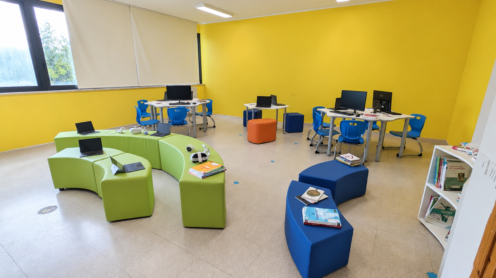 Spazio scolastico con sedute modulari verdi, computer e visori per la realtà virtuale