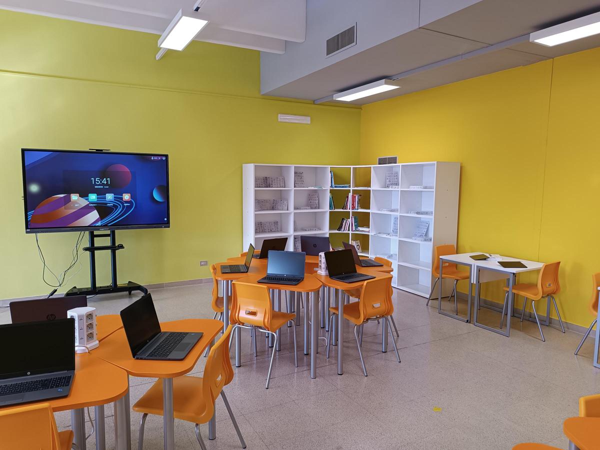Laboratorio con tavoli modulari arancioni, computer portatili e schermo digitale